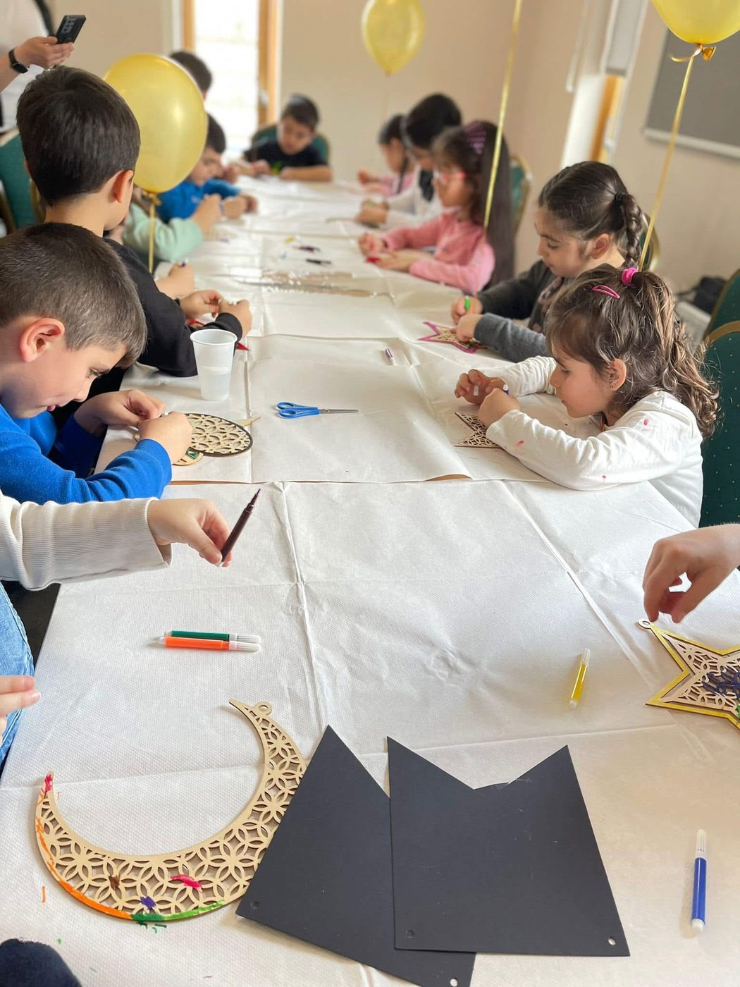 Children decorating wooden crescent and star shapes at a craft table