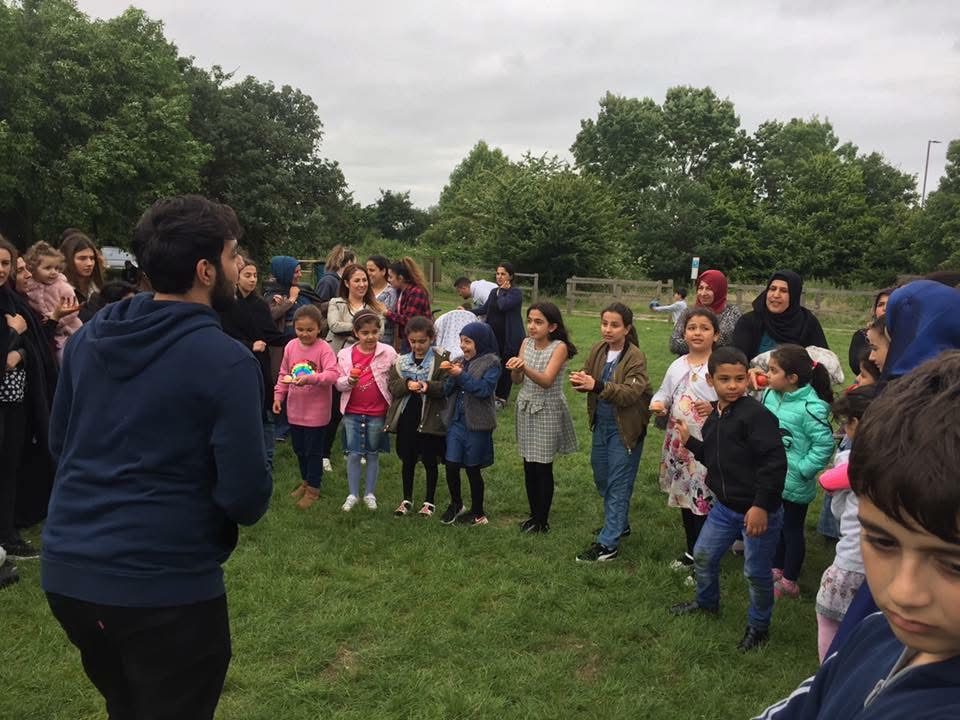 Children lined up playing an egg and spoon game at a summer picnic in the park