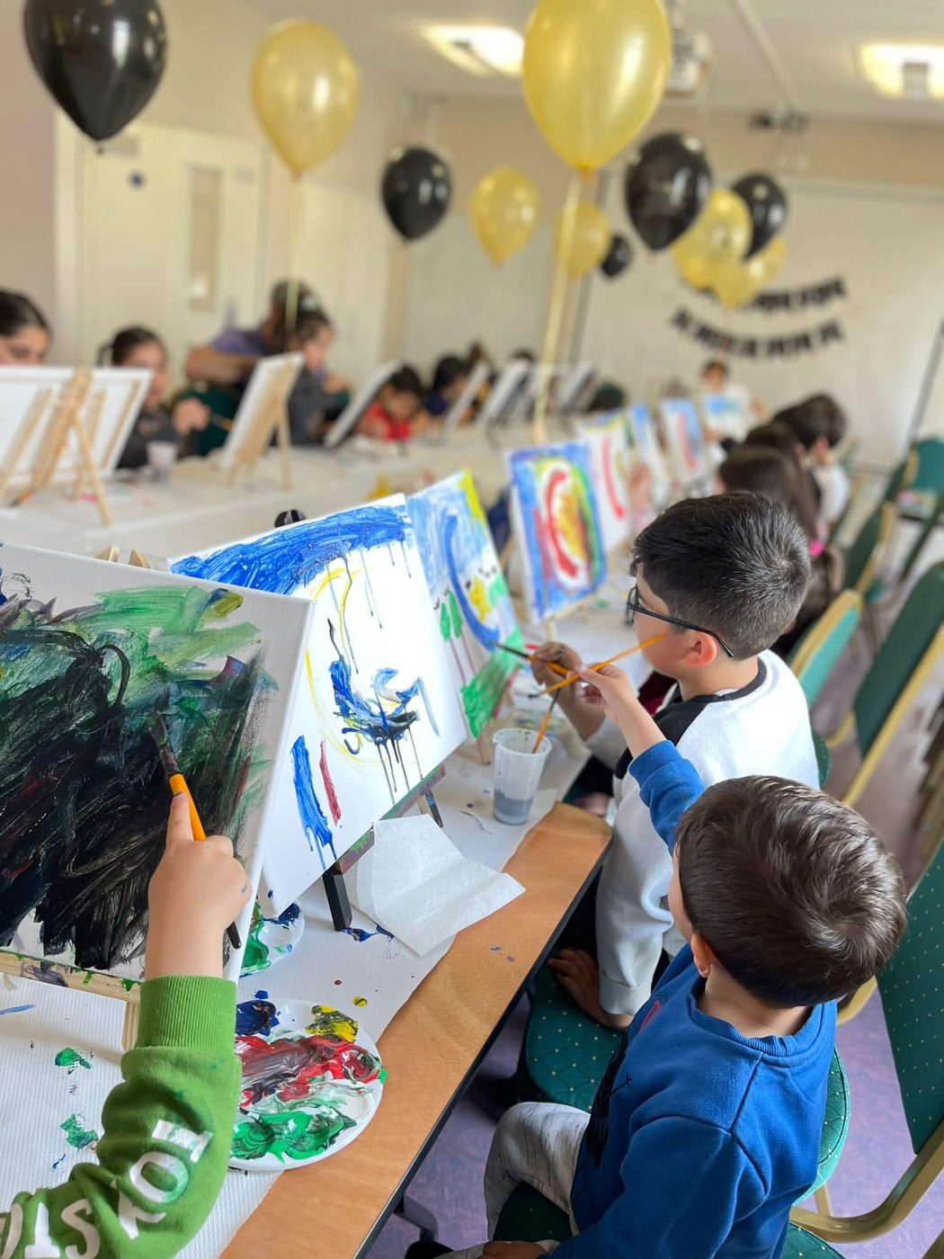 Children painting on canvases at a long table in the community centre