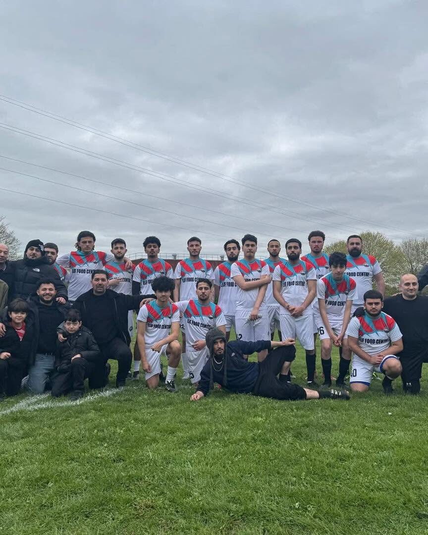 Team and supporters posing together after a match on a grass pitch