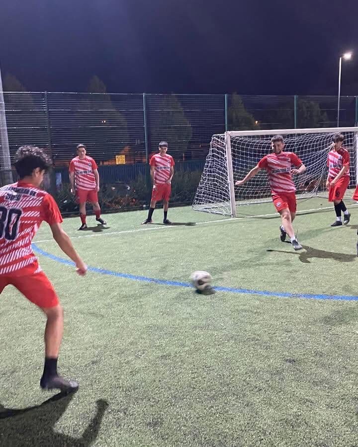 Young players in red and white kits playing an evening five-a-side game