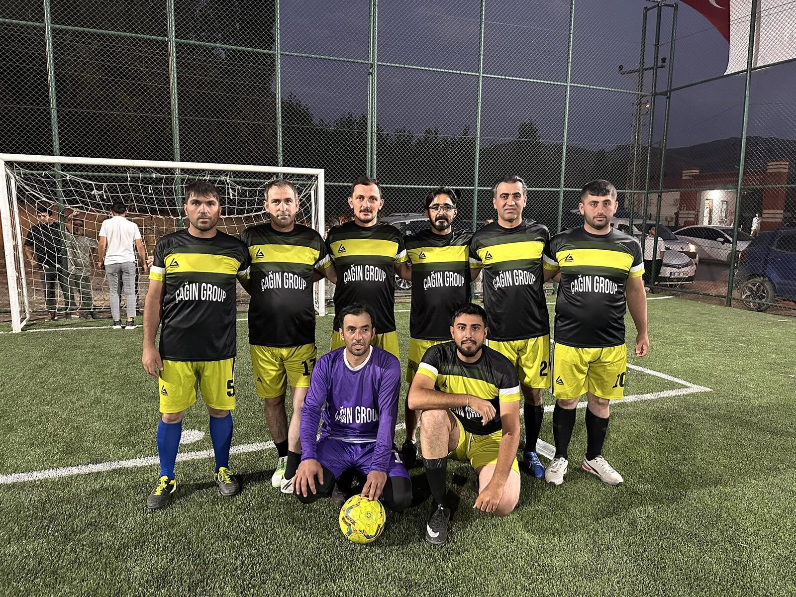 Team in black and yellow kits posing in front of the goal on the village pitch