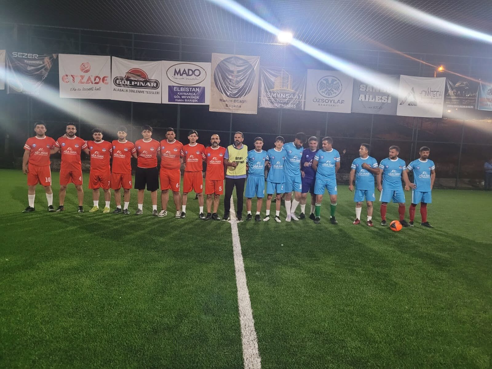 Red and blue teams standing together at the centre line under floodlights